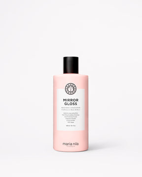 En flaska Maria Nila Mirror Gloss-balsam i en ljusrosa flaska med svart lock och en vit etikett, placerad mitt på en ljusgrå bakgrund.