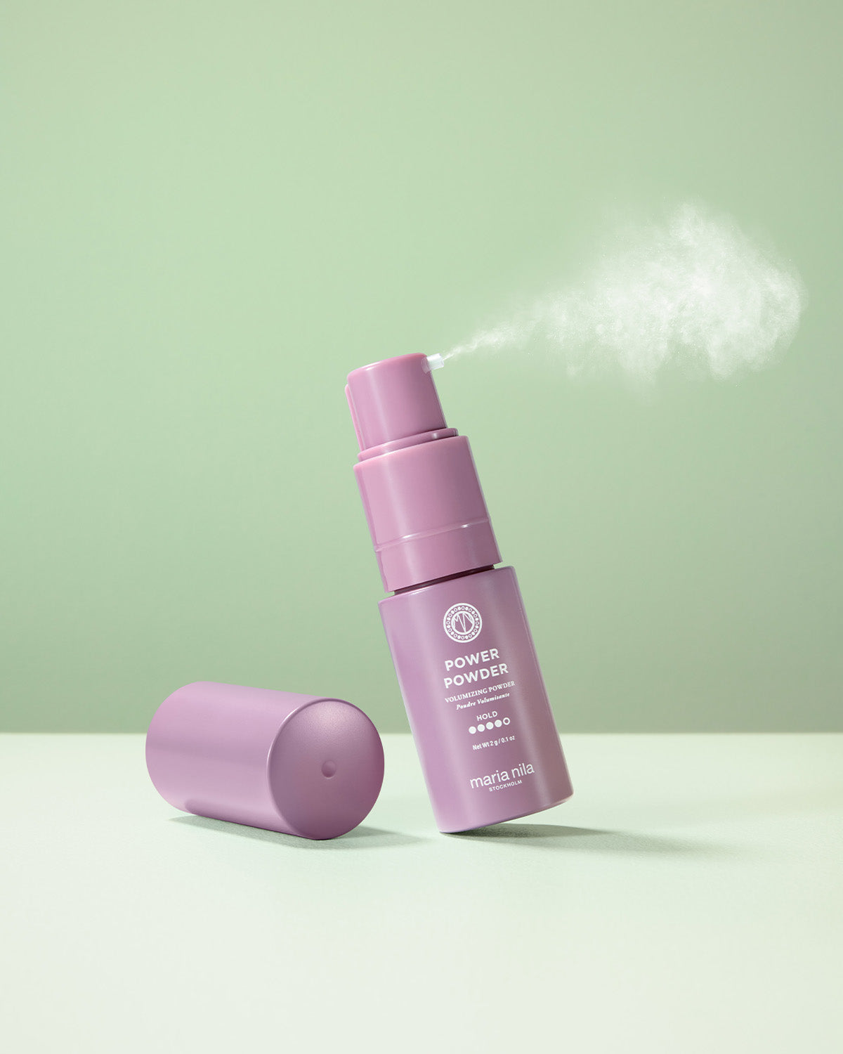 Lila flaska med Maria Nila Power Powder på grön bakgrund som sprayar en lätt vitt pulver